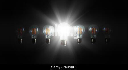 An illuminated or glowing  lightbulb among other unlit bulbs on dark background represents new idea, innovation, creativity, understanding, knowledge, Stock Photo