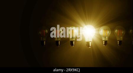 An illuminated or glowing  lightbulb among other unlit bulbs on dark background represents new idea, innovation, creativity, understanding, knowledge, Stock Photo