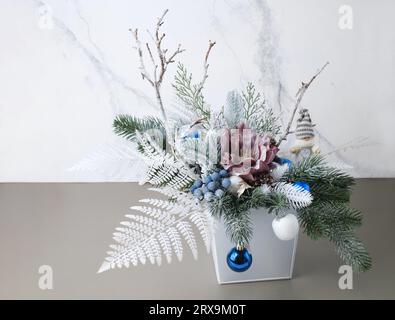 Christmas composition in box with spruce, fern for table decoration. Snowy bunches with blue bobbles, elf in beautiful packaging, assembled by a Stock Photo