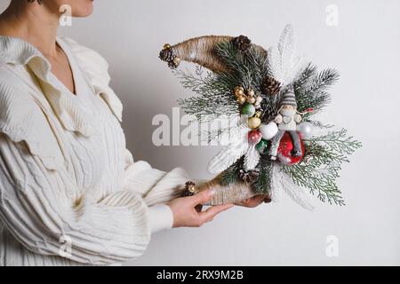 Close-up woman holding moon shape Christmas wreath with elf. The basis of the wreath is spruce branches, no waste festive decoration in female hands Stock Photo