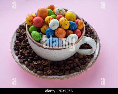 Composition with small chocolate easter eggs in cup surrounded by coffee roasted beans. Easter coffee concept. Mug full of colorful eggs on a plate wi Stock Photo