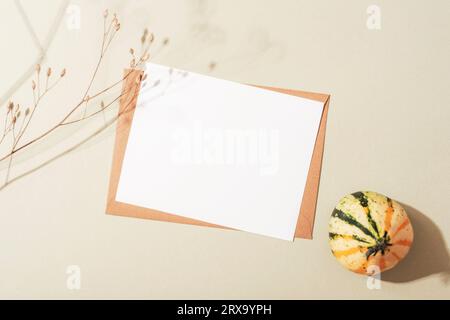 Envelope with blank card, dried flower and small pumpkin with sharp shadows on neutral background. Autumn concept. Top view, flat lay, mockup. Stock Photo