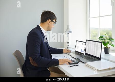 Financial accountant working in office, sitting at desk and using laptops and calculator Stock Photo