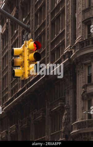 A red stop light displayed on a yellow traffic light at the intersection of a street and avenue in New York City with an old building background with Stock Photo