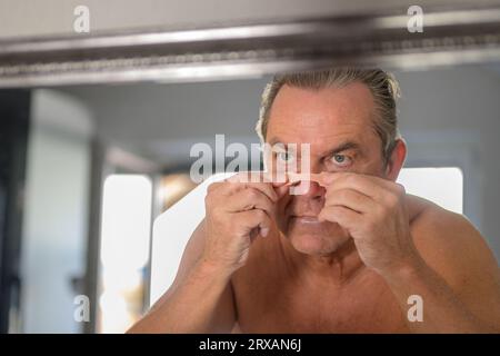 Middle aged man applying a nose tape while looking in the mirror in the bedroom Stock Photo