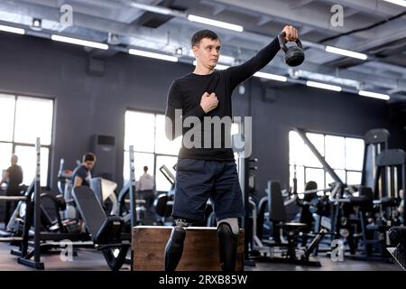 active ambitious sportsman raising kettlebell, working out with sport equipment, tool, close up side view photo. blurred background, motivation, stren Stock Photo