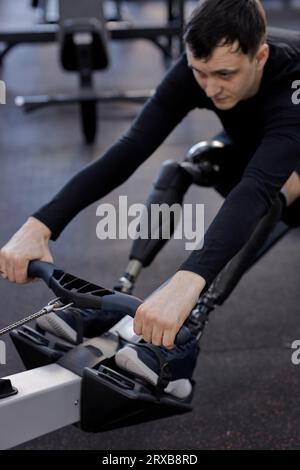 motivated sportsman with artificial legs limb working out in gym on rowing machine, lifestyle spare time, health and body care, cropped photo. focus o Stock Photo