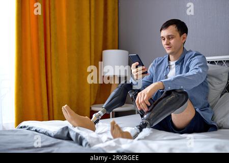 man with artificial leg prosthesis using smartphone, browsing web or watching movie at home. Handicapped young Caucasian guy checking social media, ty Stock Photo