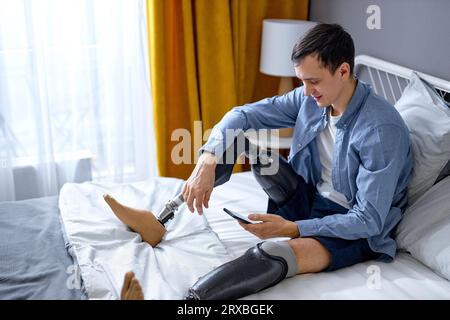 man with artificial leg prosthesis using smartphone, browsing web or watching movie at home. Handicapped young Caucasian guy checking social media, ty Stock Photo