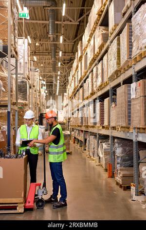 caucasian men warehouse workers with hand pallet jack lift stand having talk, temwork. hand pallet truck and male mover. Workers in uniform with cargo Stock Photo