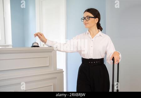 European Young Businesswoman Ringing Bell At Reception Counter Indoors Stock Photo