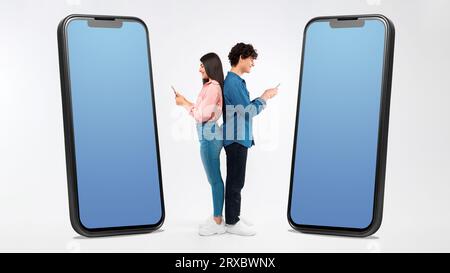 Young Teen Couple Using Smartphones Standing Near Huge Phones, Studio Stock Photo