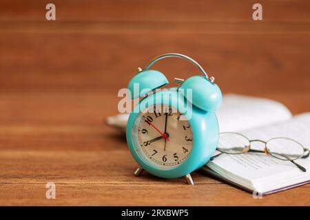 Colorful alarm clock, books, glasses on wooden table on wood grain background. back to school concept Stock Photo