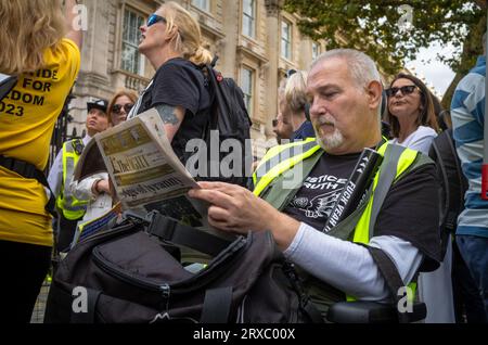 A middle-aged man in a wheelchair at a demonstration by conspiracy theorists in outside Downing Street in Whitehall, London, reads a copy of 'The Ligh Stock Photo