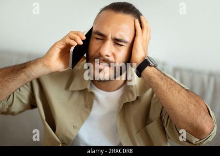 Stressed guy sitting on couch, having conversation on phone Stock Photo