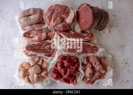 Assorted raw meats including sausage, pork, lamb, beef, chicken, and brisket on a metal table. The table is next to a marble one. Stock Photo