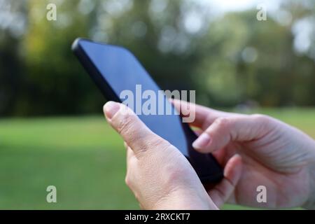 Smartphone in female hands close up on park background. Woman using mobile phone outdoors Stock Photo