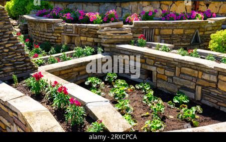 Landscaping with retaining walls and flowerbeds in house backyard, landscape design of upscale home garden with stone walls in summer. Flowers and pla Stock Photo
