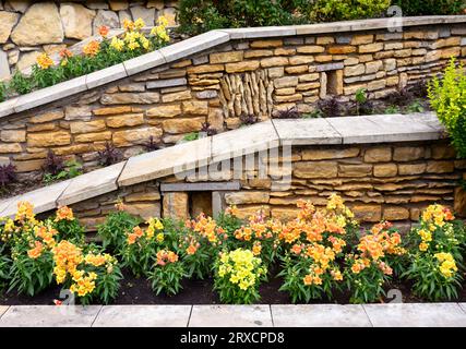 Landscaping with retaining walls and flowerbeds in house backyard, landscape design of upscale home garden with stone walls in summer. Flowers and pla Stock Photo