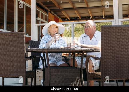 Happy mature middle aged couple talking, woman showing off her hat, flirting. On a date in a cafe. Stock Photo