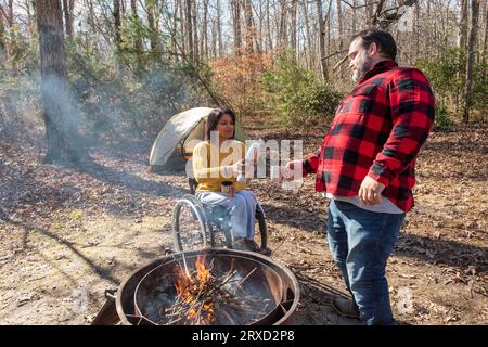 An outdoorsy couple shares a hot beverage to stay warm at their campsite. Both are disabled but love the outdoors. Stock Photo