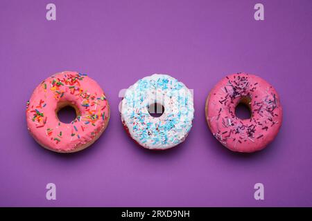 Sweet glazed donuts decorated with sprinkles on purple background, flat lay. Tasty confectionery Stock Photo