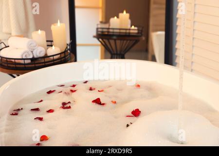 Bath tub with foam and rose petals in bathroom Stock Photo