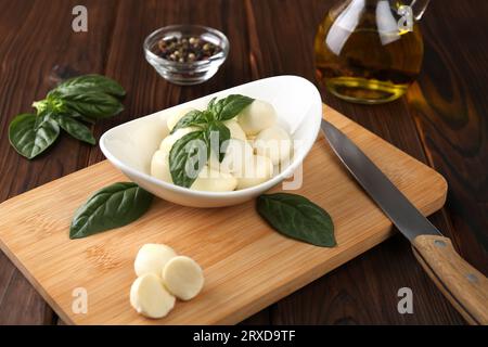 Tasty mozarella balls, basil leaves and knife on wooden table Stock Photo