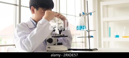 Children scientist learning on biology and chemistry in the laboratory. A STEM education learning concept. An Asian student boy using microscope in a Stock Photo