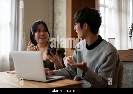 A cheerful Asian woman enjoys talking and sharing her ideas with her friend while sitting in a coffee shop together. Lifestyle concept Stock Photo