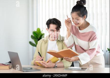 A friendly and kind Asian female friend is helping her friend with math lessons, tutoring, and preparing for the exam with her friend at home. Educati Stock Photo