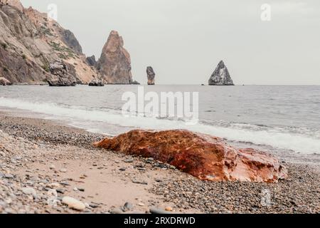 Large red jasper rock on the beach, with the sea in the background. Big Red Jasper Stone Close Up Stock Photo