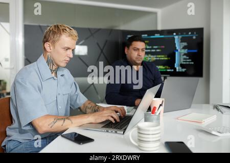 Serious software developer coding on laptop at office desk Stock Photo