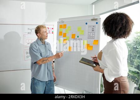 Managers discussing ideas on stickers when standing at whiteboard in office Stock Photo