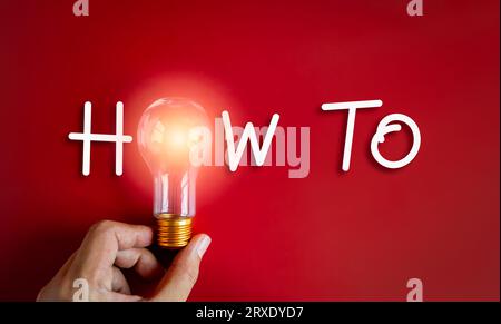 How to concept. Text "HOW TO" decoration with with glowing light from lightbulb, holding by hand on red background. Business solution, creativity and Stock Photo