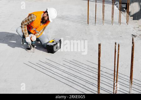 Repairman worker in uniform and helmet working with cordless screwdriver and tool box. Stock Photo
