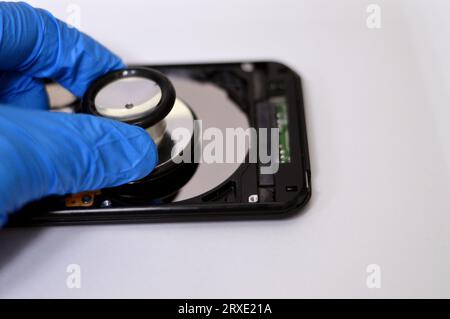 A medical stethoscope on HDD platters and spindle motor, hard disk drive disassembled damaged components, computer maintenance, running diagnostics, r Stock Photo