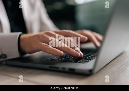 Close-up cropped shot of unrecognizable businessman in suit working on laptop computer by window. Closeup male fingers typing buttons on laptop Stock Photo