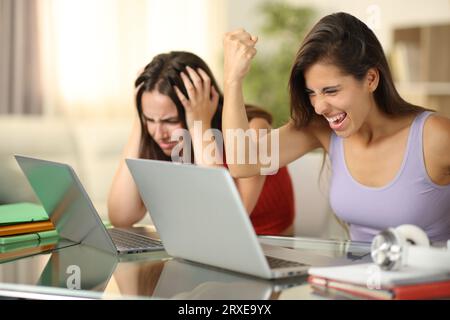 Student celebrating success and another one complaining checking laptops at home Stock Photo