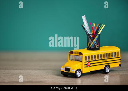 Toy school bus, back to school concept. Creative composition of yellow school bus carrying variety of school supplies. Stock Photo
