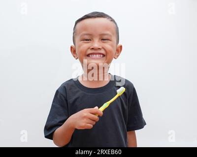 little asian boy holding a toothbrush while smiling on white background with copy space. children's dental health concept Stock Photo