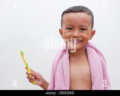 little asian boy holding a toothbrush while smiling on white background with copy space. children's dental health concept Stock Photo