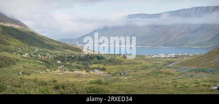 panorama of Isafjordur harbor and town in Iceland with farms in the foreground and a cruise ship and misty clouds in the background Stock Photo