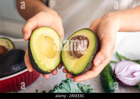 Avocado halves in a female hand in the kitchen. Stock Photo