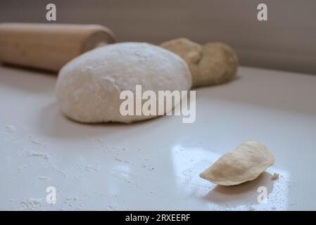 Process of making vareniki. One ready in front of a big piece of dough Stock Photo