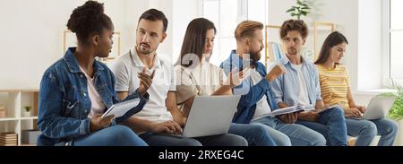 Group of diverse people sitting in office, discussing work and using cell phones and laptops Stock Photo