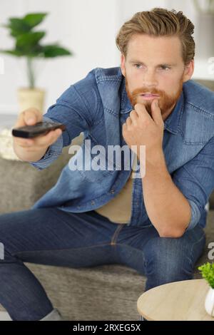 young man changes the channels on the remote control Stock Photo