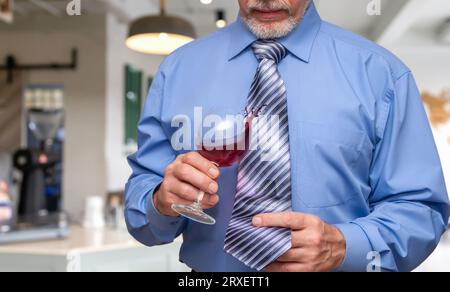 A man holding a wine glass in his hand and is letting some of vine drip onto his tie. Stock Photo