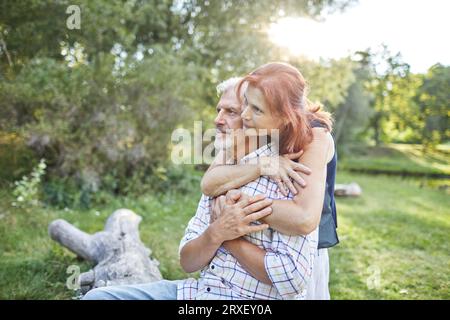 senior woman hugging gray-haired man sitting in the park Stock Photo