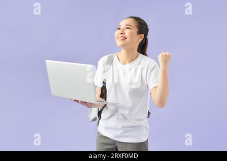 Young woman student backpack hold pc isolated on violet wall background studio portrait. Stock Photo